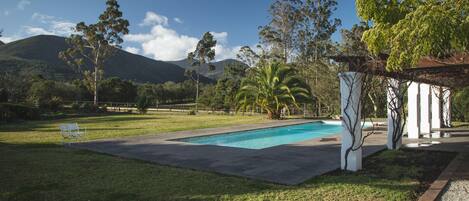 Una piscina con césped, árboles y un edificio con columnas.