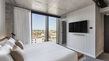 Een moderne hotelkamer met een groot bed, een flatscreen televisie aan de muur en een stadszicht door ramen van de vloer tot aan het plafond.