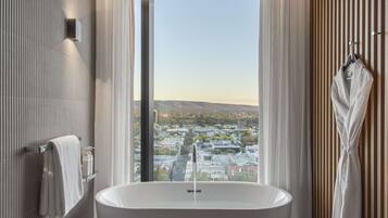 Un baño moderno con una bañera independiente, un ventanal con cortinas y vistas a un paisaje urbano.