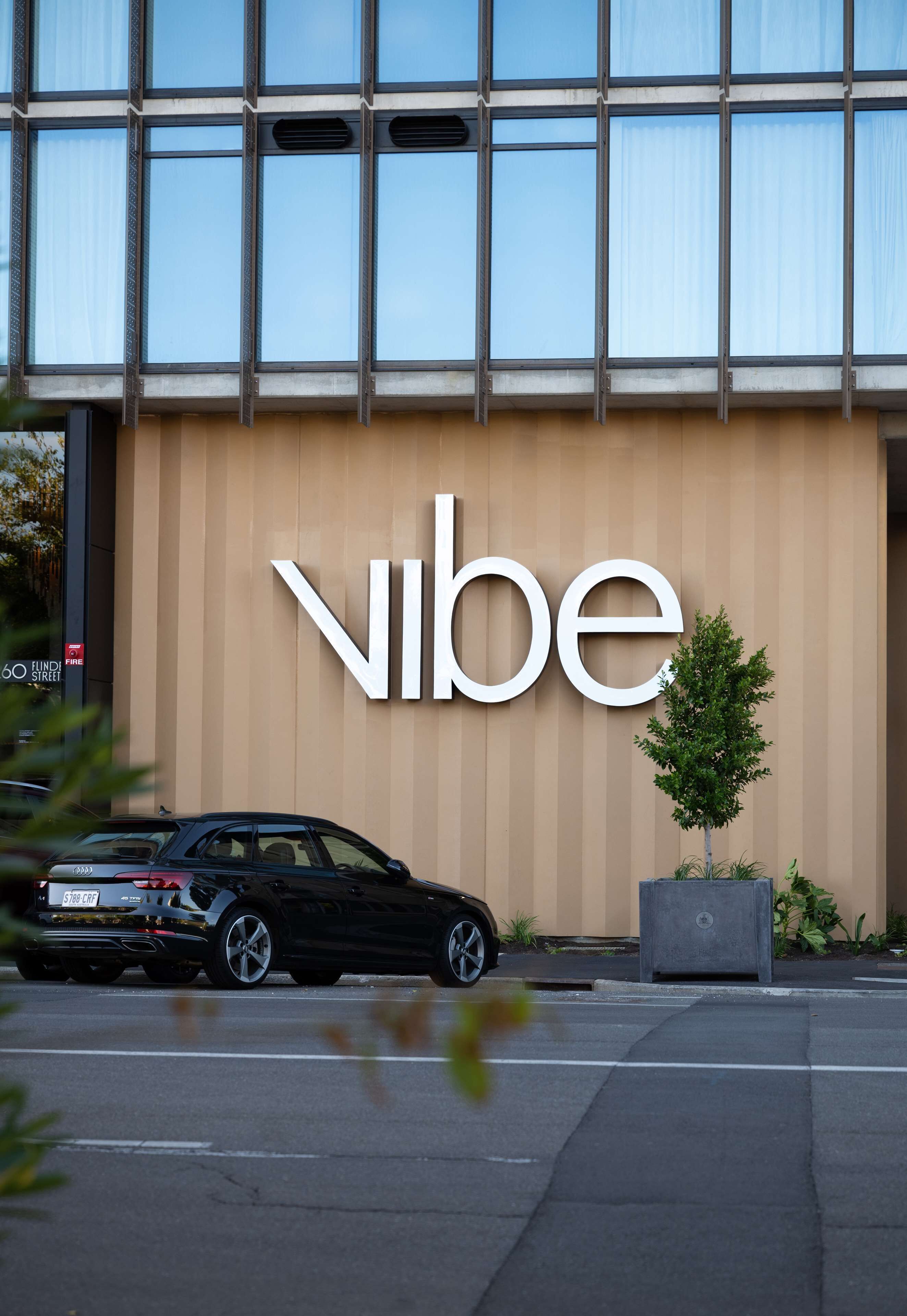 A building with a large 'Vibe' sign, a black car parked in front, and a small tree in a planter.