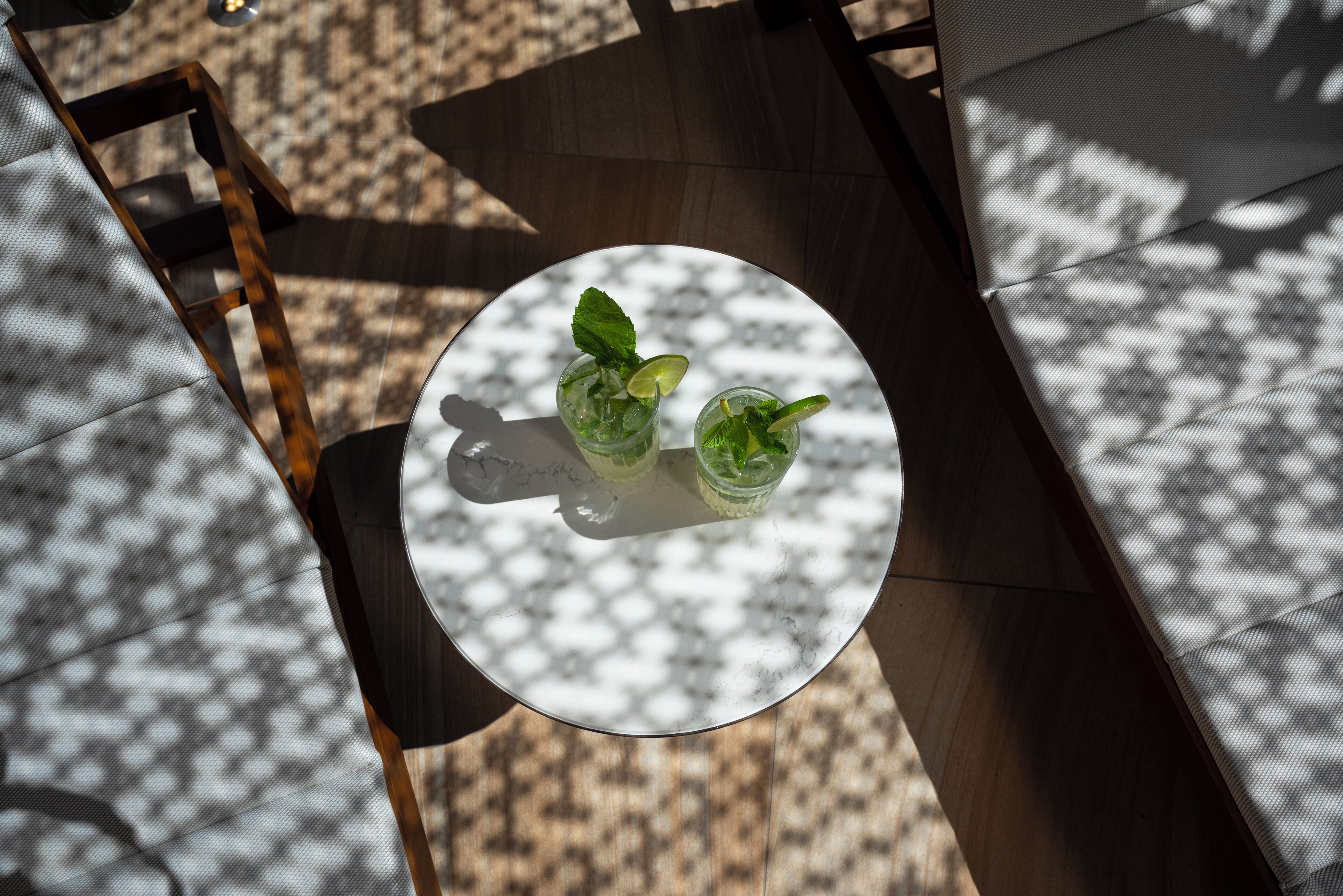 A round table with two glasses of a beverage, a chair, and a patterned floor.