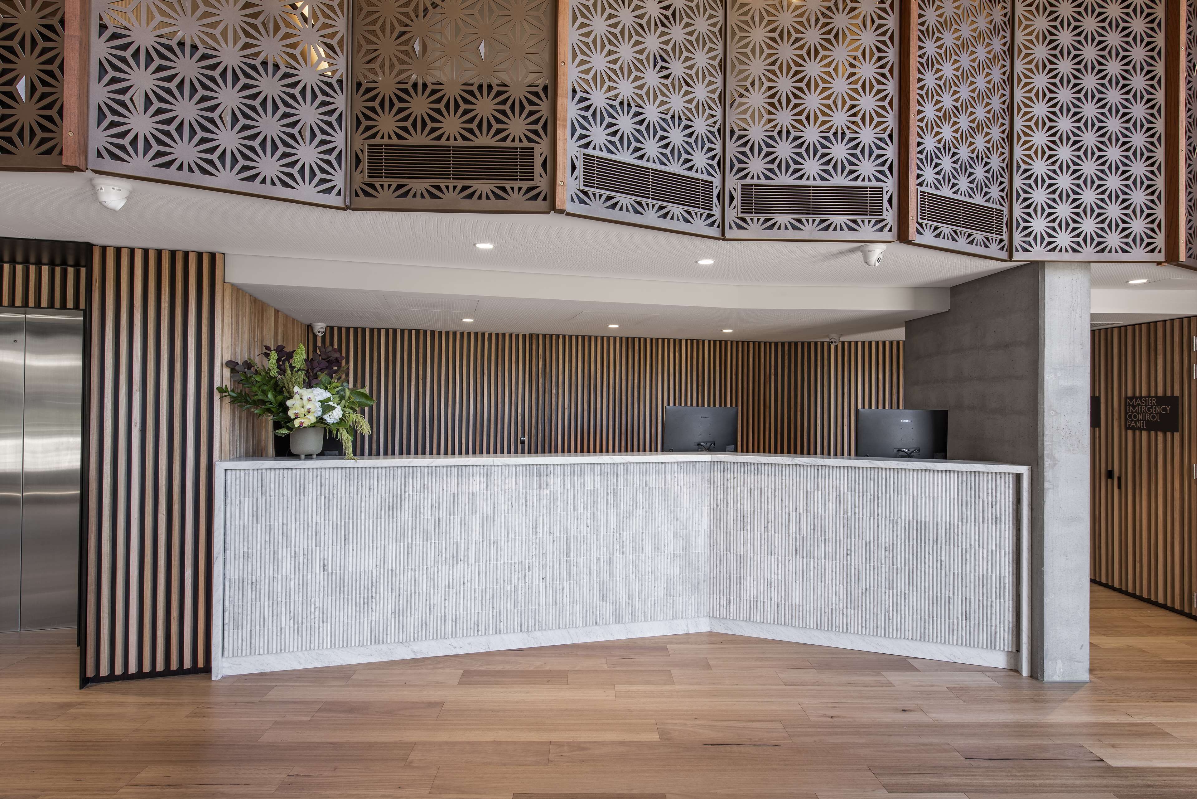 A reception desk with a modern design, flanked by wooden paneling and a decorative screen.