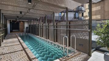 A modern indoor pool area with a clear water feature, metal railings, and a patterned floor.