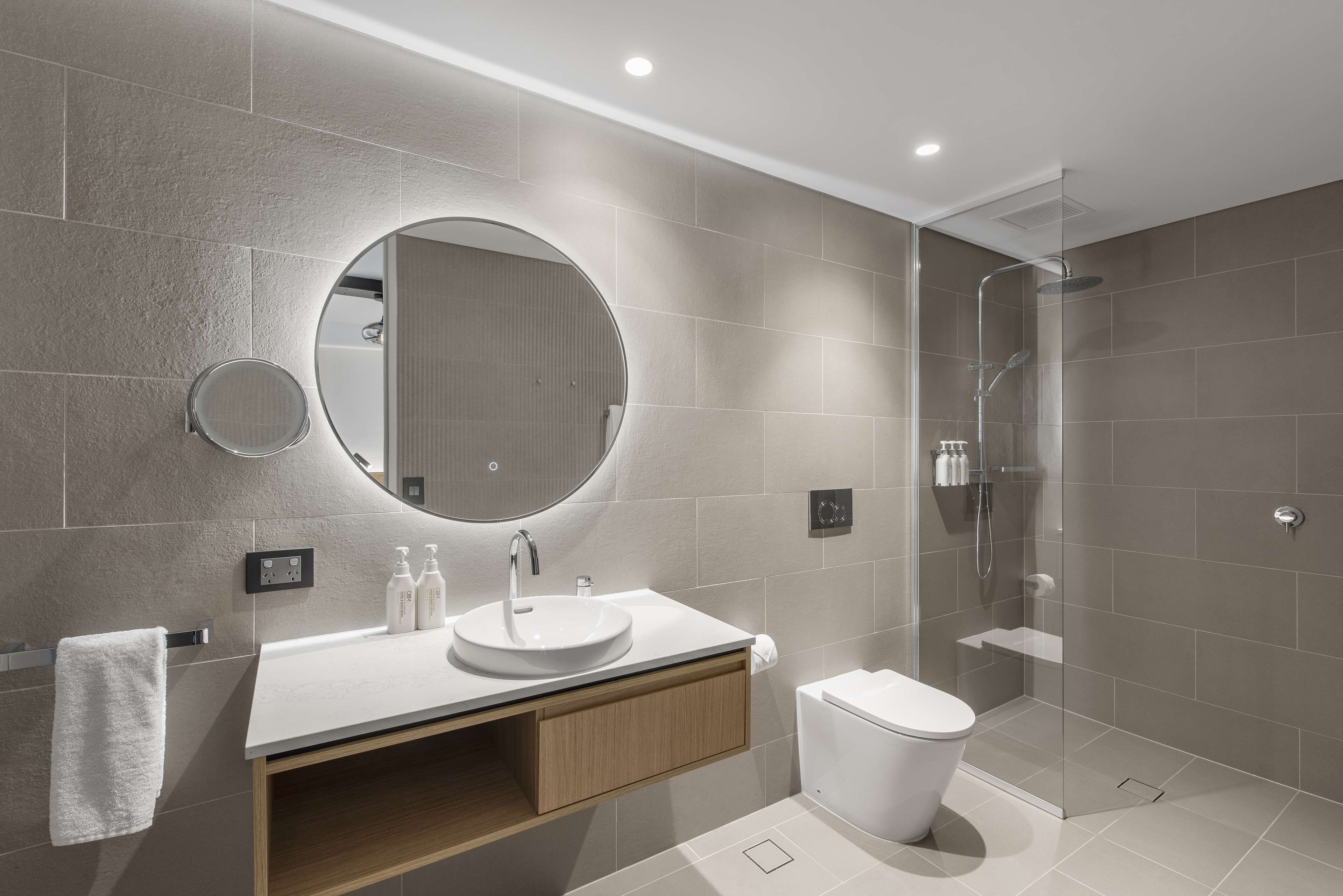 A modern bathroom with a round mirror, a sink, and a toilet.