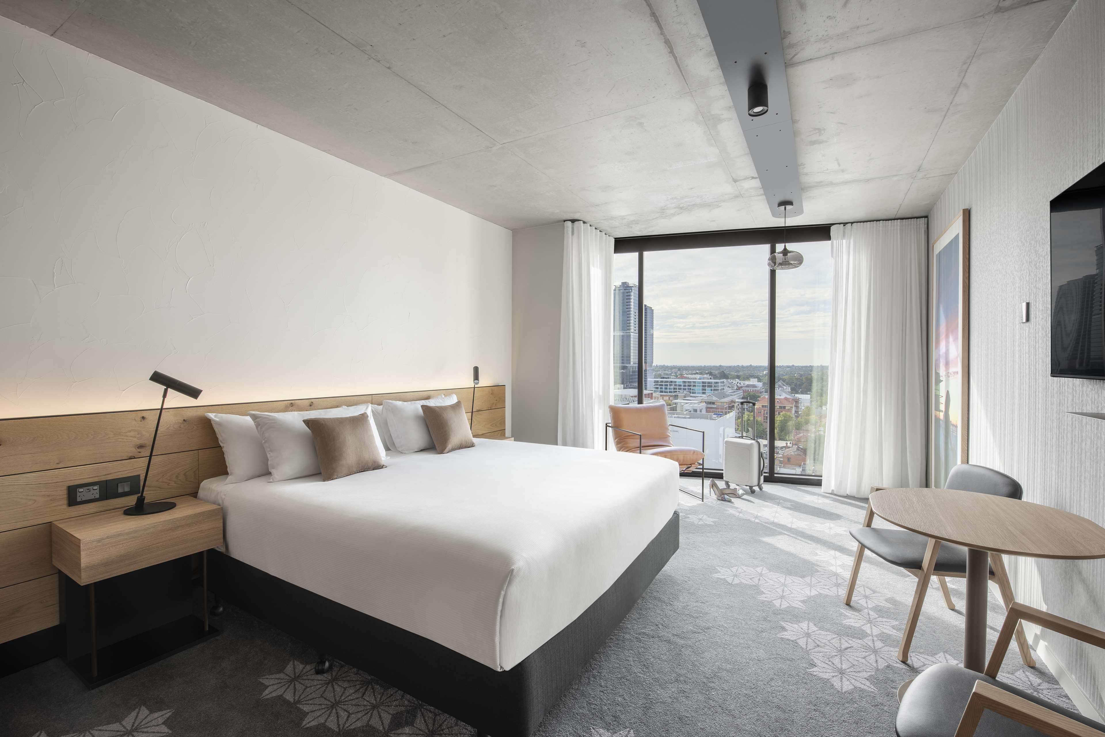 Una habitación de hotel moderna con una cama grande, un escritorio y vistas de la ciudad a través de amplios ventanales.
