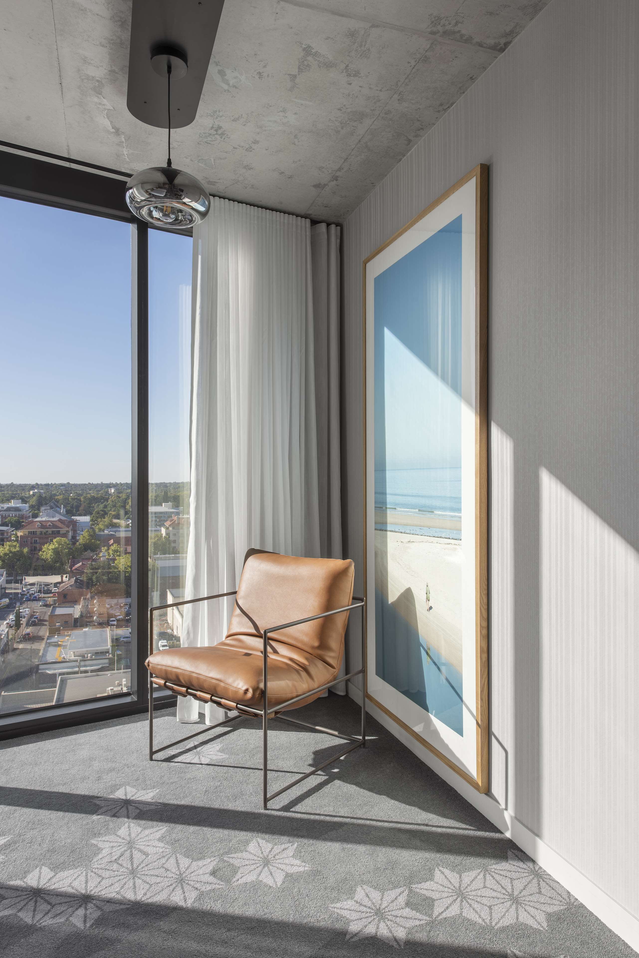 A modern room with a large window, a leather chair, a framed artwork, and a patterned carpet.