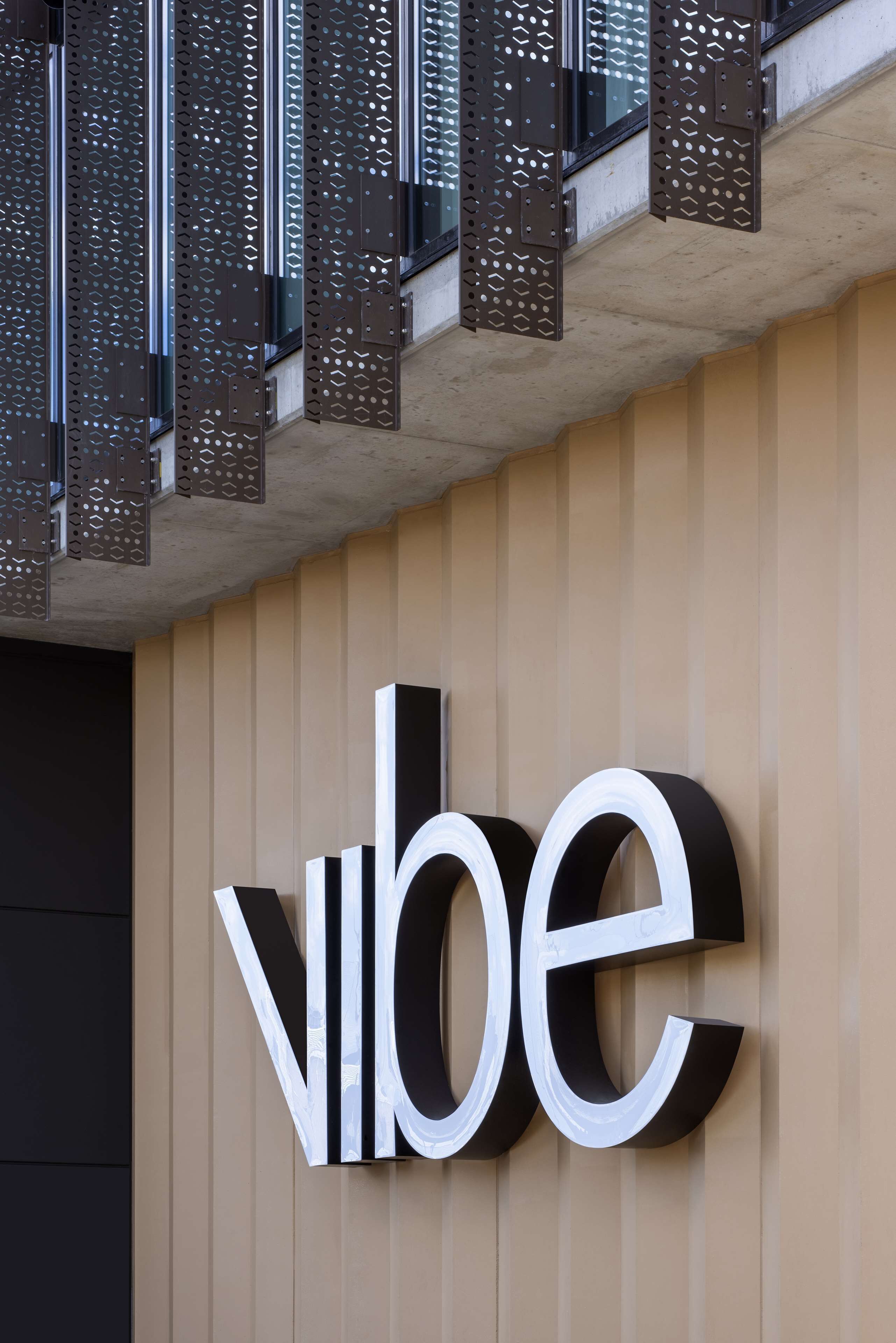 Fachada de edificio con un gran letrero que dice 'VIBE' en letras negritas blanco y negro.