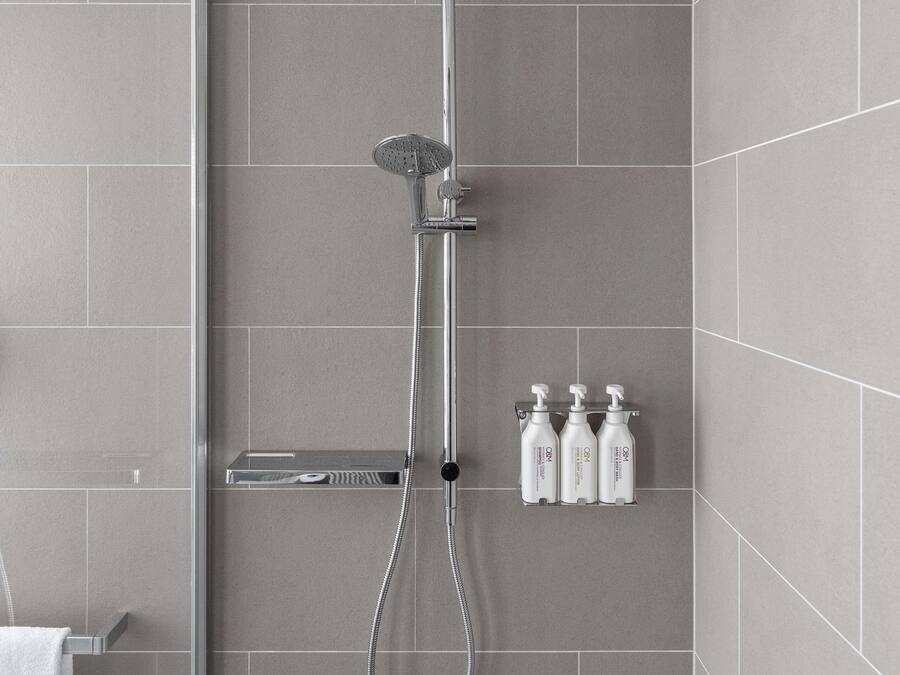 Ducha moderna con cabezal de ducha de lluvia, cabezal de ducha manual y un accesorio de ducha manual. Hay tres botellas de champú y acondicionador sobre una repisa.