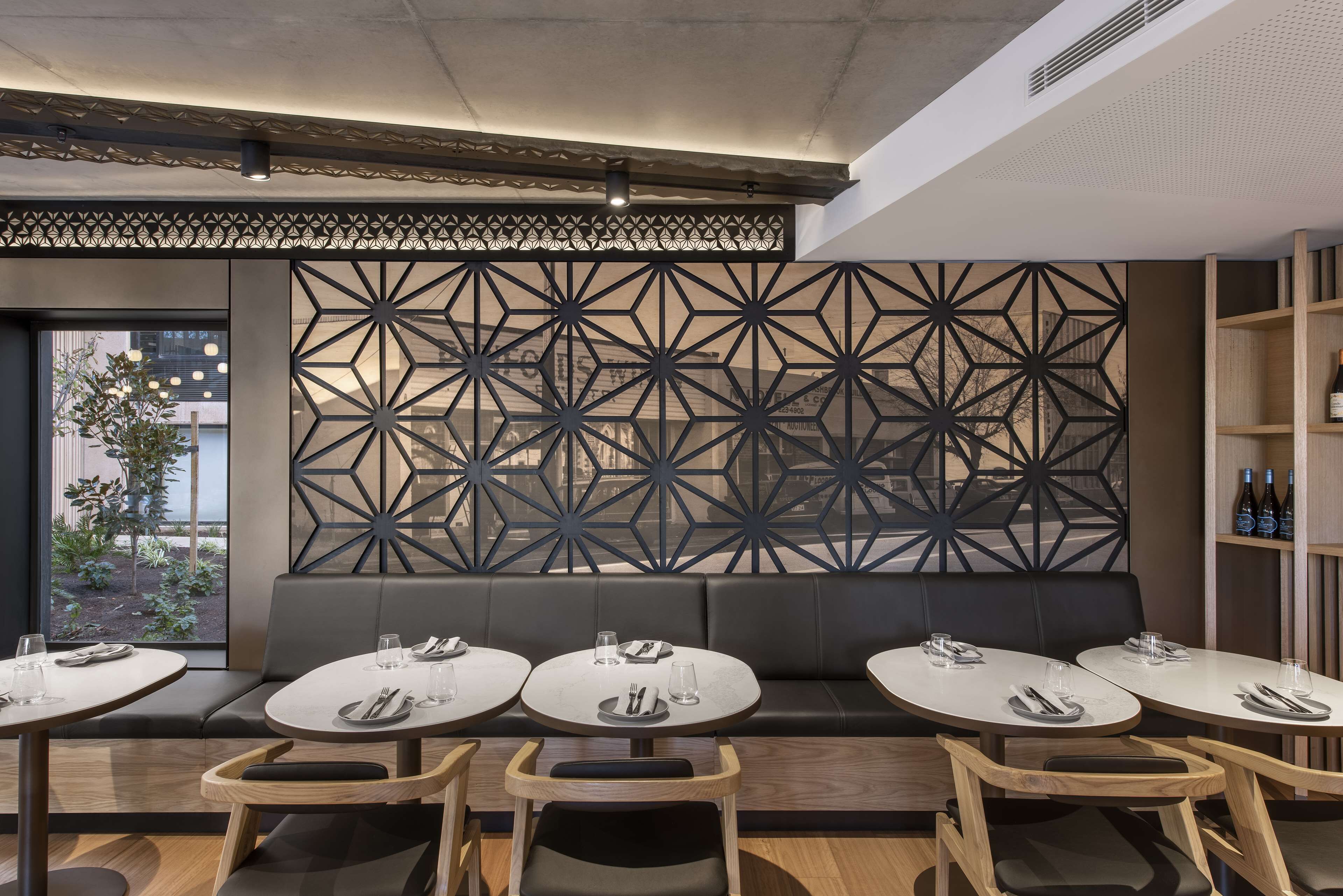 Un intérieur de restaurant moderne avec un décor mural géométrique, des tables rondes et un espace détente agrémenté d’un banc noir rembourré.