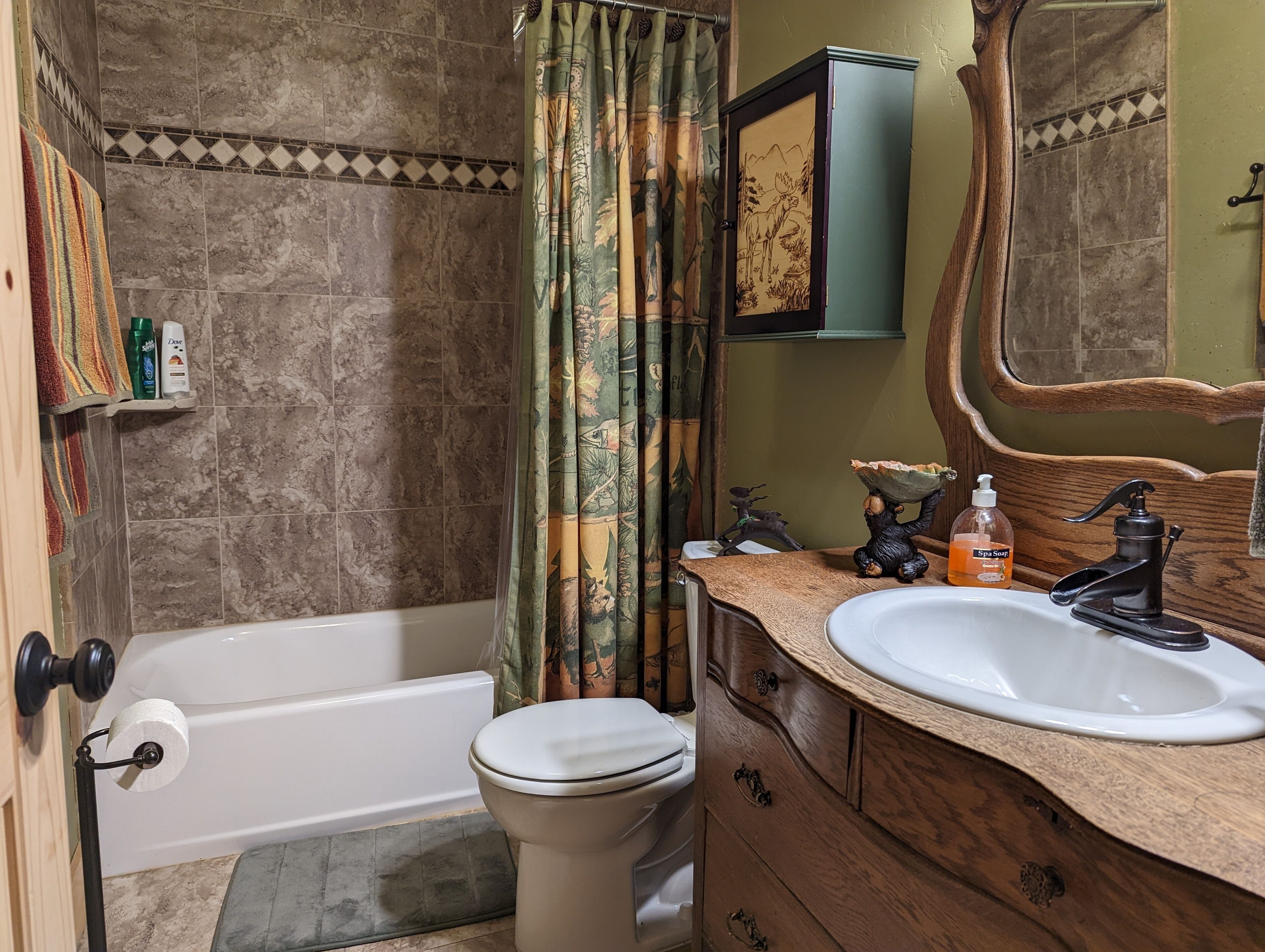 A bathroom with a bathtub, toilet, wooden vanity, and a mirror.