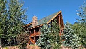 A lodge with a stone chimney, wooden deck, and a grassy yard with trees.