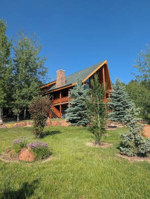 Eine Lodge mit einem Steinkamin, einer Holzterrasse und einem Rasenstück mit Bäumen.