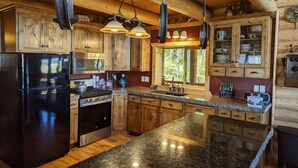 A modern kitchen with wooden cabinets, a black refrigerator, stainless steel appliances, granite countertops, and pendant lighting.