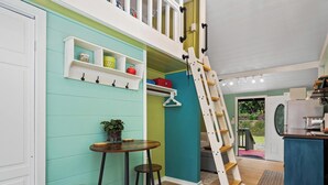 A room with a teal wall, wooden bar stools, a ladder, and a kitchen area with a blue cabinet. - Adorable Cottage w/ Jungle & Mountain Vibes (Holualoa)