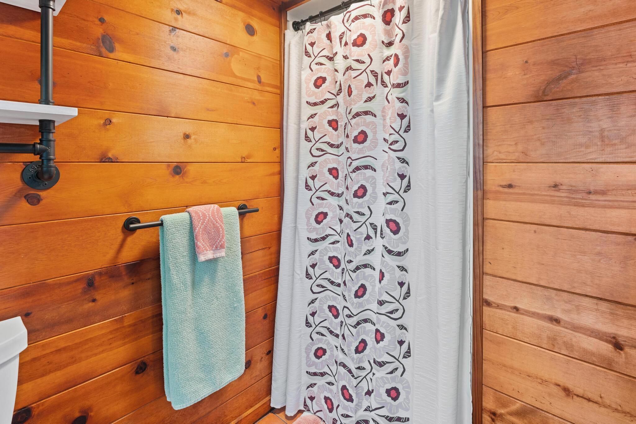 A wooden interior with a towel rack holding two towels, a shower curtain with a floral pattern, and a visible showerhead.