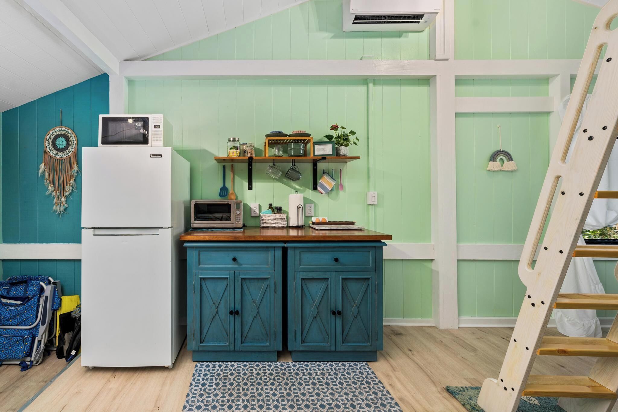 A kitchen with teal cabinets, a white refrigerator, and a microwave. There is a wooden ladder leaning against the wall.
