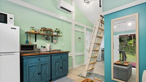A kitchen with teal cabinetry, a microwave, a toaster, and a wooden shelf with kitchen items. - Adorable Cottage w/ Jungle & Mountain Vibes (Holualoa)