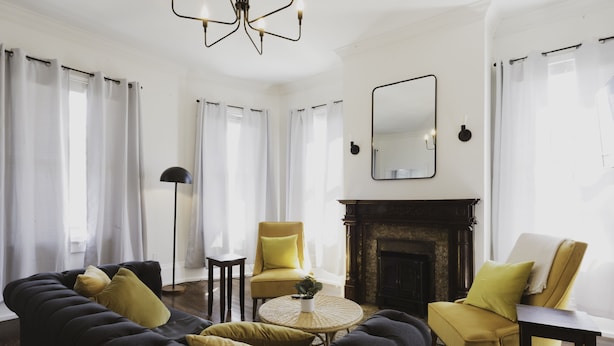 Un salon avec un canapé foncé, des fauteuils jaunes, une table basse ronde et une cheminée.