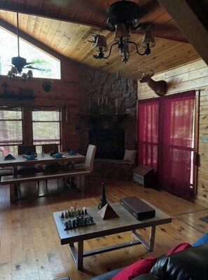 Cozy cabin-style room with a stone fireplace, wooden ceiling, and large window, perfect for relaxation and quiet activities.
