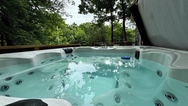 Un jacuzzi con múltiples chorros, rodeado de exuberante follaje y una terraza de madera.