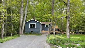 A cabin with a gravel driveway, surrounded by lush greenery and trees.