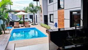 A modern outdoor pool area with a hammock, lounge chairs, and a car parked nearby. - Beautiful Townhouse with 3 suites, Pool and Garage for 4 Cars (Florianópolis)