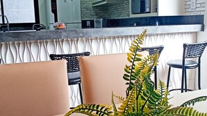 A modern kitchen with white cabinets, a microwave, and a refrigerator. There is a dining area with a table, chairs, and a potted plant. - Beautiful Townhouse with 3 suites, Pool and Garage for 4 Cars (Florianópolis)