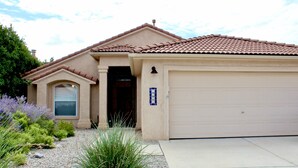 A residential house with a beige facade, a tiled roof, a garage, and a small garden with various plants. - Prime Northeast Heights Location - 3 Bedroom - 2.3 mi to Balloon Fiesta Park! (Albuquerque)