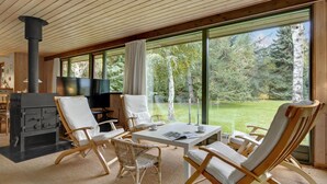 Ein gemütliches Zimmer mit Kamin, bequemen Sitzgelegenheiten und großen Fenstern mit Blick ins Freie.