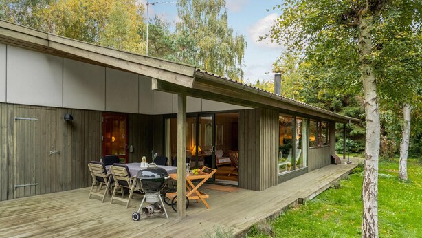 Ein modernes Haus mit überdachter Terrasse, Essbereich und Blick auf die umliegenden Bäume.