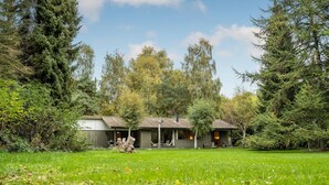 Eine Holzhütte mit Ziegeldach, umgeben von dichtem Wald und einer grünen Wiese davor.