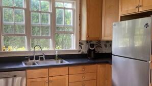A kitchen with wooden cabinets, a stainless steel refrigerator, a double sink, and a window with a view of greenery. - 1-bedroom in the Borough, just steps to the water (Stonington)