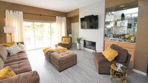 A living room with a sofa, ottoman, and armchair, a flat-screen TV, a fireplace, and a glass display cabinet. - 224 Calle Florista, Laguna De LaPaz (La Quinta)