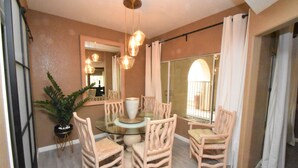 A dining area with a glass table surrounded by wooden chairs, a potted plant, and a large mirror on the wall. - 224 Calle Florista, Laguna De LaPaz (La Quinta)