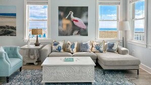 A spacious living room with a large window, a ceiling fan, and a sofa with decorative pillows. - Pointe West Family Beach + 2 Resort Pools (Galveston)