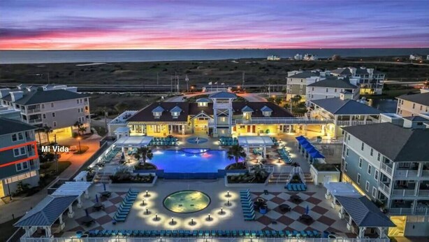 A resort with a swimming pool, outdoor seating, and a view of the ocean at dusk. - Pointe West Family Beach + 2 Resort Pools (Galveston)