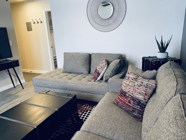 A modern living room with a sectional sofa, a flat-screen TV, and a round mirror on the wall.