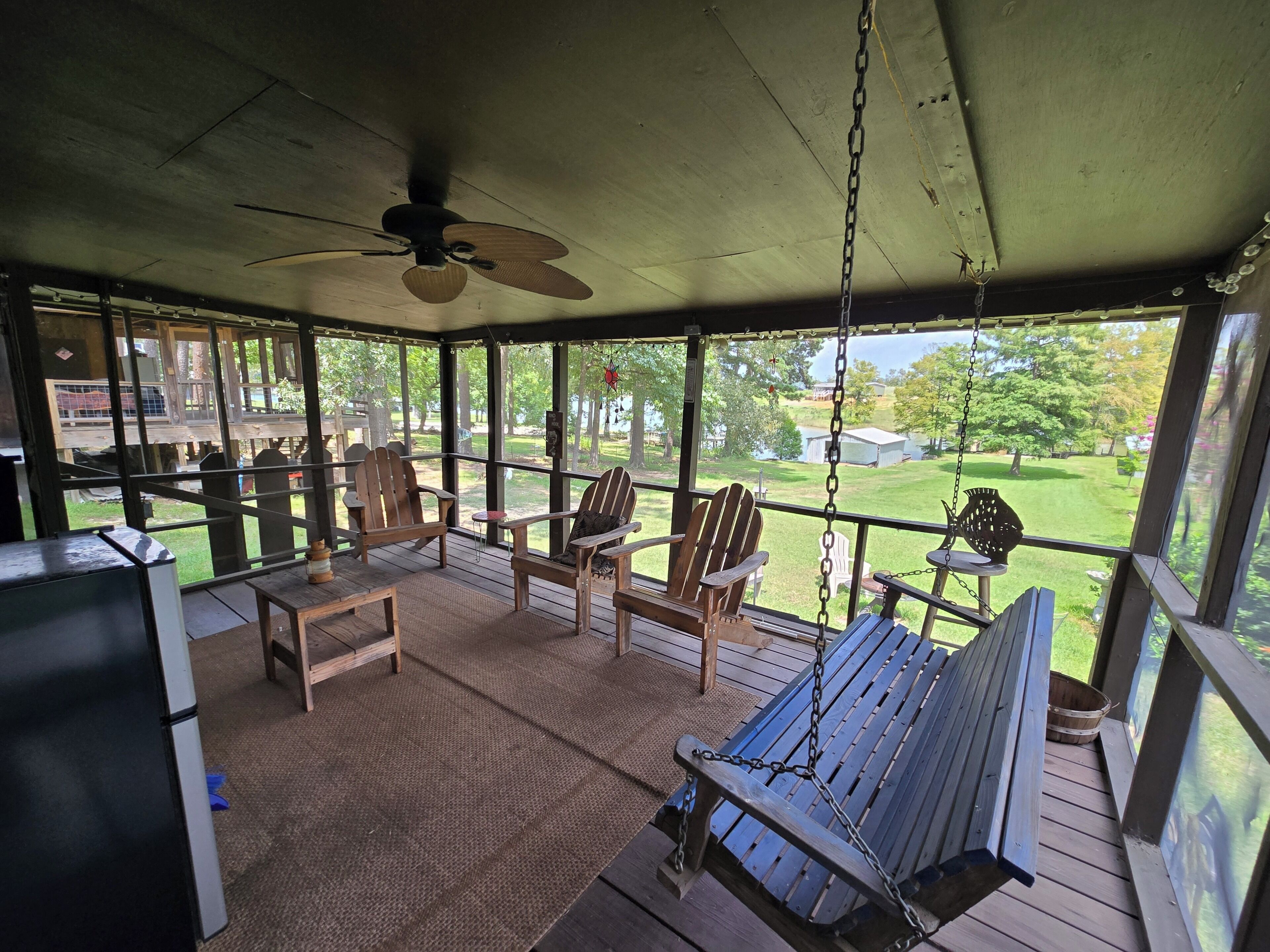 A covered outdoor seating area with chairs and a swing, overlooking a grassy yard.