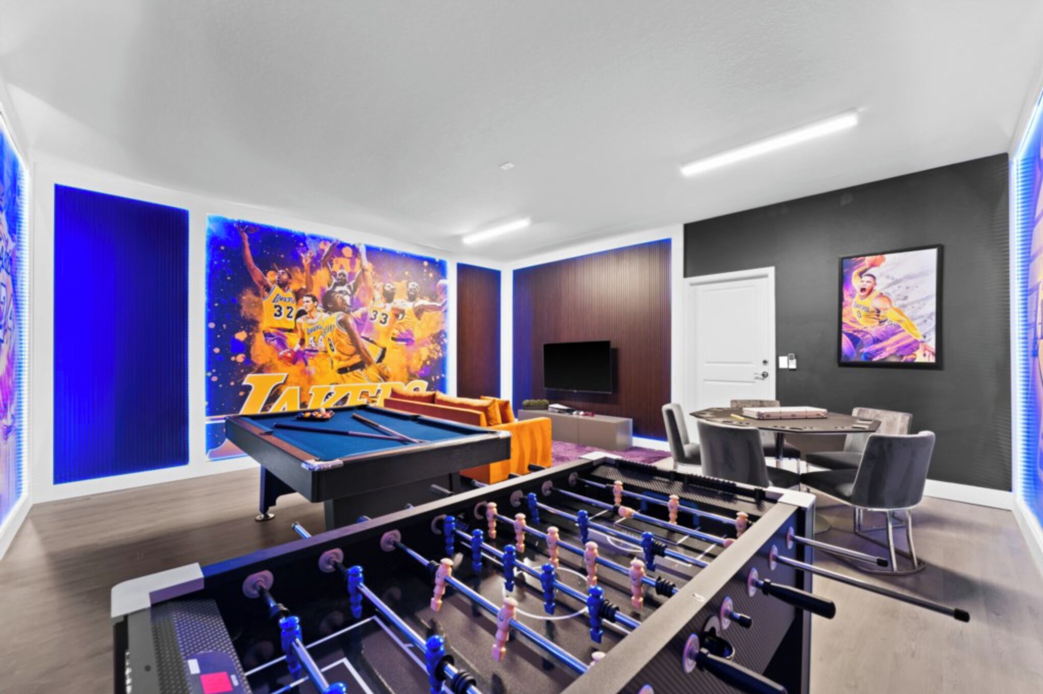 A room with a foosball table, a pool table, and a TV.