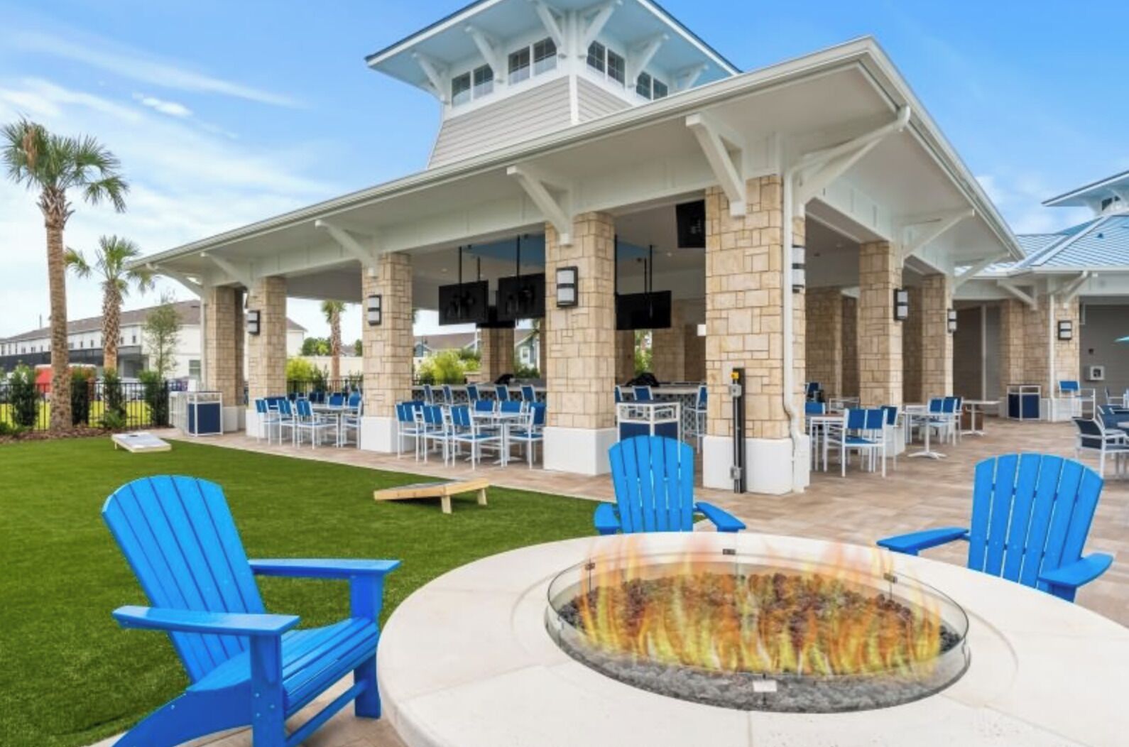 A covered outdoor seating area with fire pit, blue chairs, and tables.