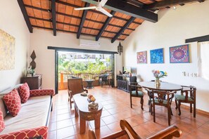 A spacious living area with a high ceiling, a dining table, and a sofa with red cushions.