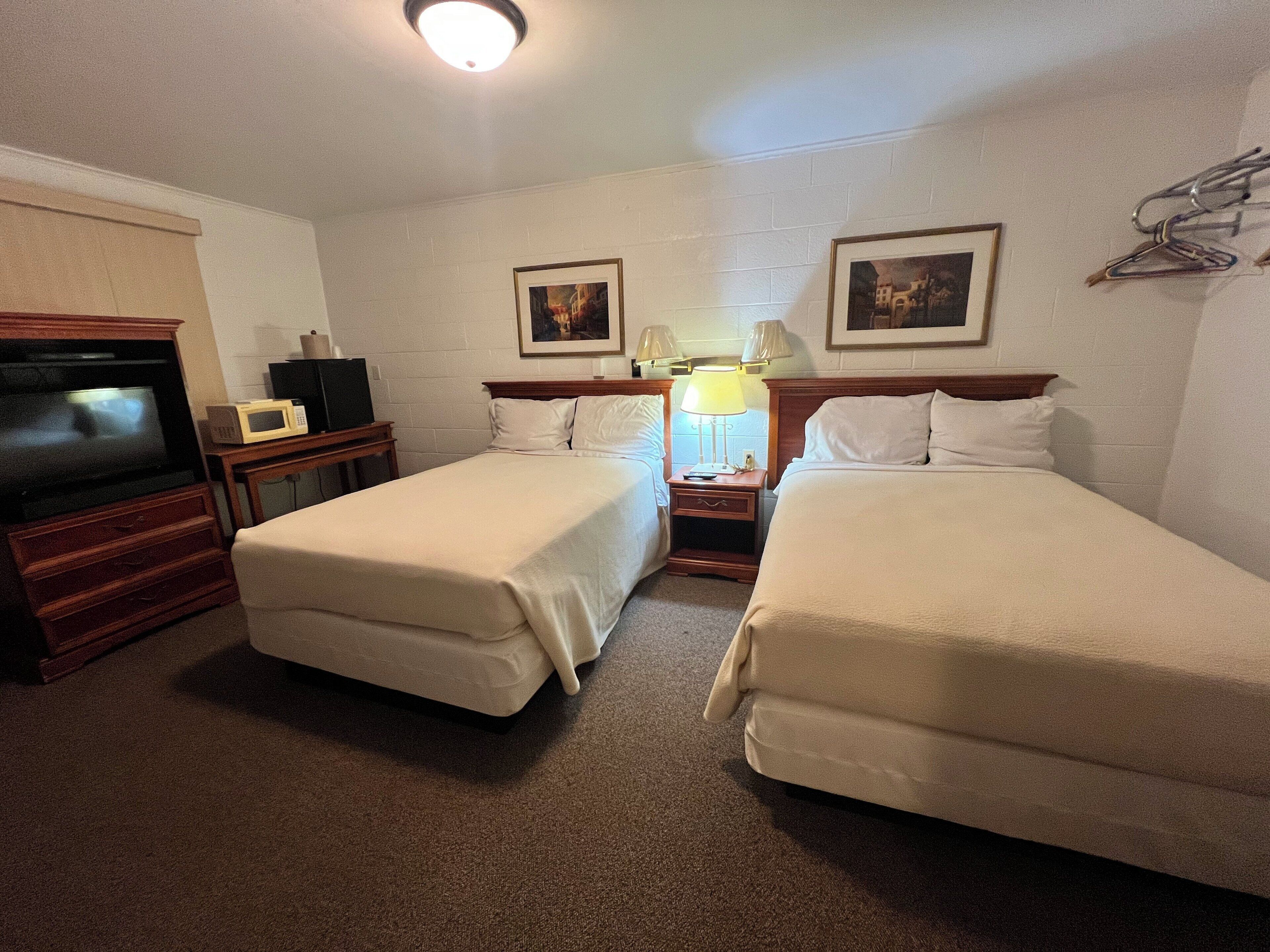A hotel room with two single beds, a TV, a microwave, and a bedside table with a lamp.