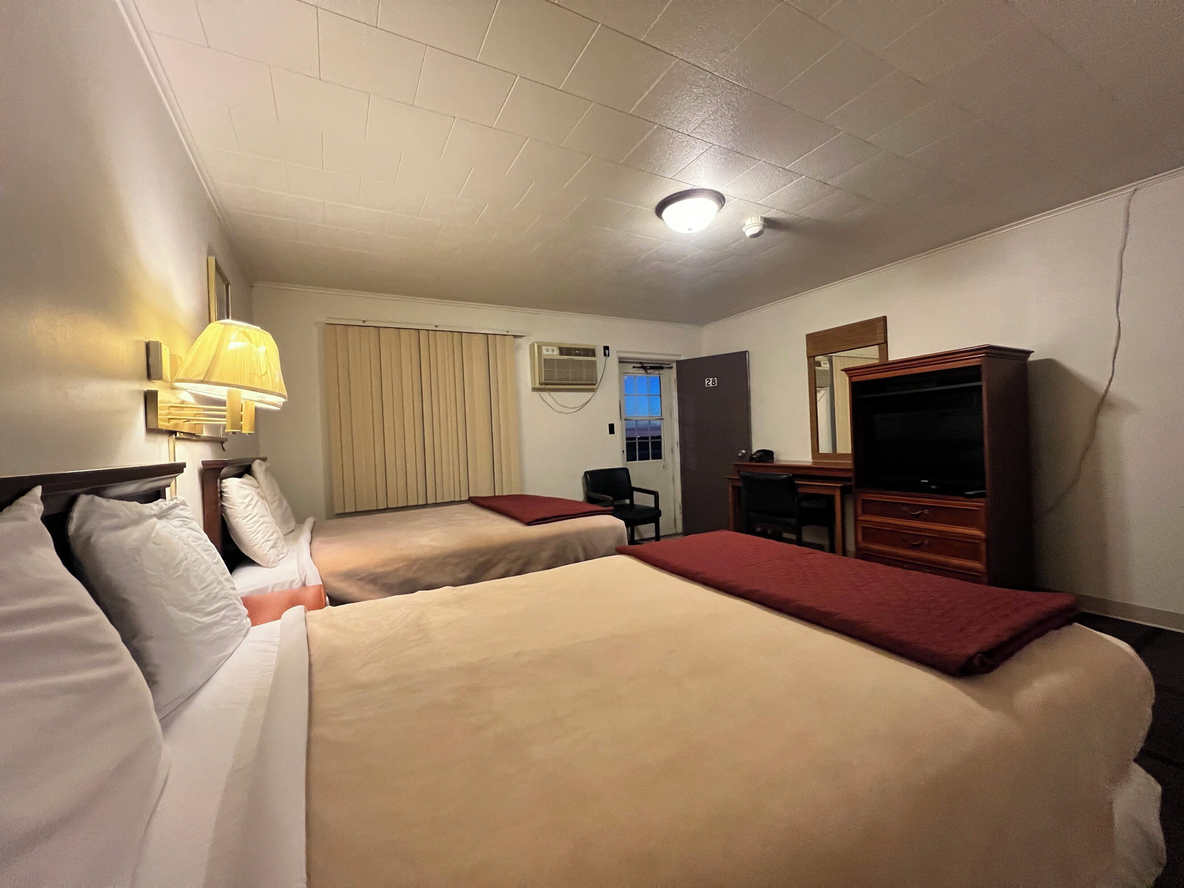 Habitación de hotel con dos camas, un escritorio, una silla, un televisor y una ventana con cortinas.