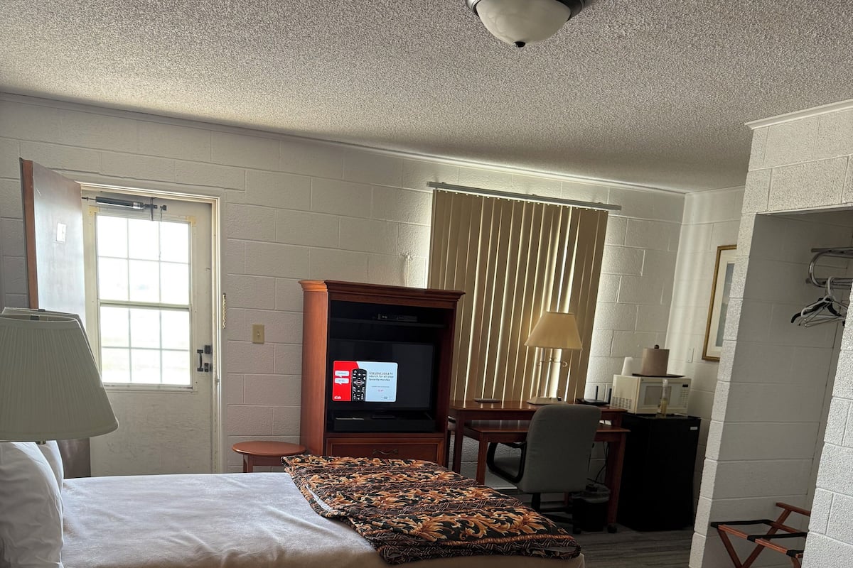 Quarto de hotel com duas camas, televisão, escrivaninha e um computador, além de uma janela.