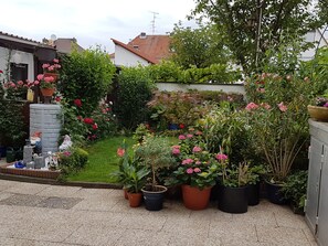 En have med plantekrukker, blomster, en stenvæg og et lille bassin.