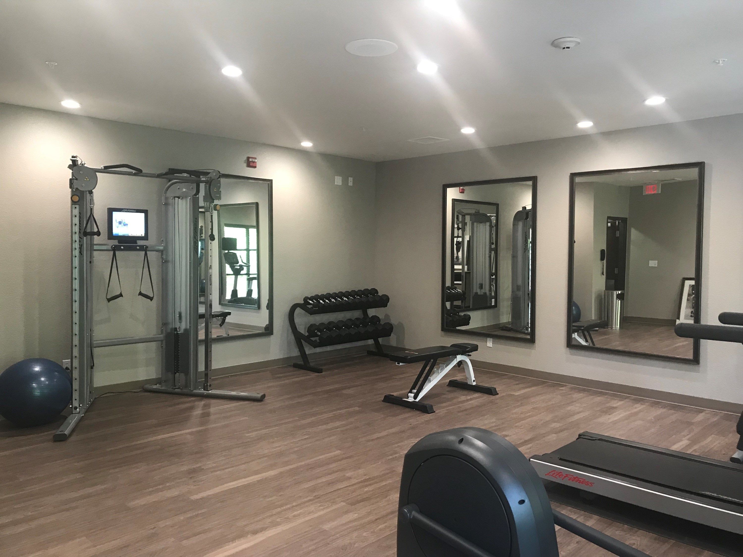 Un gimnasio con equipo de ejercicio, espejos y una cinta de correr.