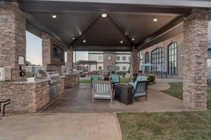 Une terrasse extérieure avec des piliers en pierre, un barbecue et des sièges.