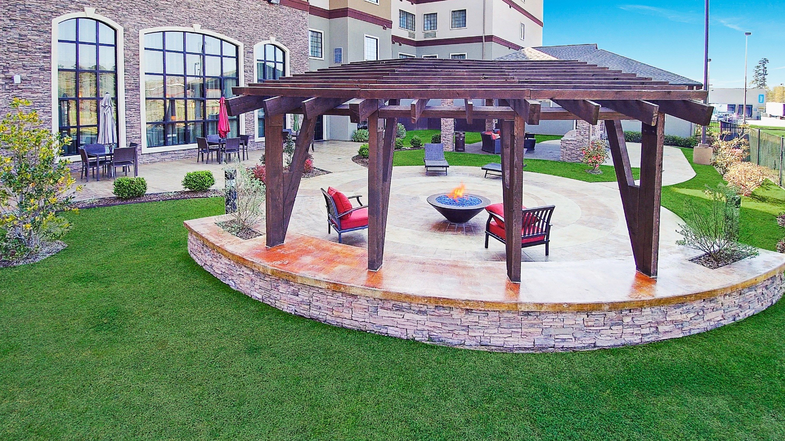 A covered outdoor seating area with a fire pit, surrounded by stone walls and a grassy lawn.