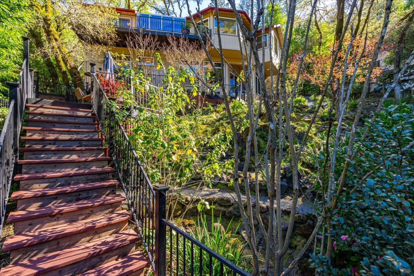 A wooden staircase with a metal railing leading to a building with a blue roof.