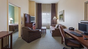 A hotel room with a sofa, armchair, desk with a computer, TV, and a small table. - 1 Bedroom | Free Breakfast + 24h Business Center (Tallahassee)